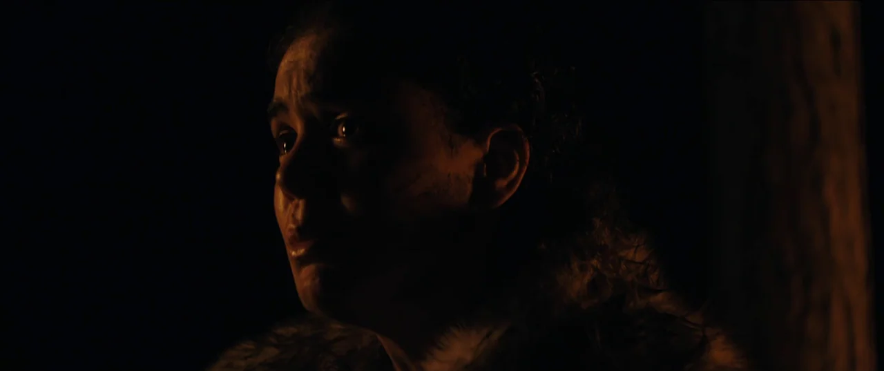 Out of Darkness (2022) movie still: closeup — A person is positioned in a dark environment with light hitting only one side. The subject stares…