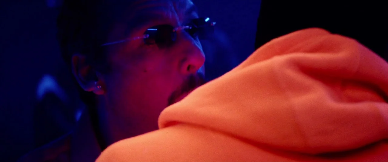 Uncut Gems (2019) movie still: closeup — A dimly lit nightlife setting with deep blue atmosphere and intense color contrast. A man in dark…