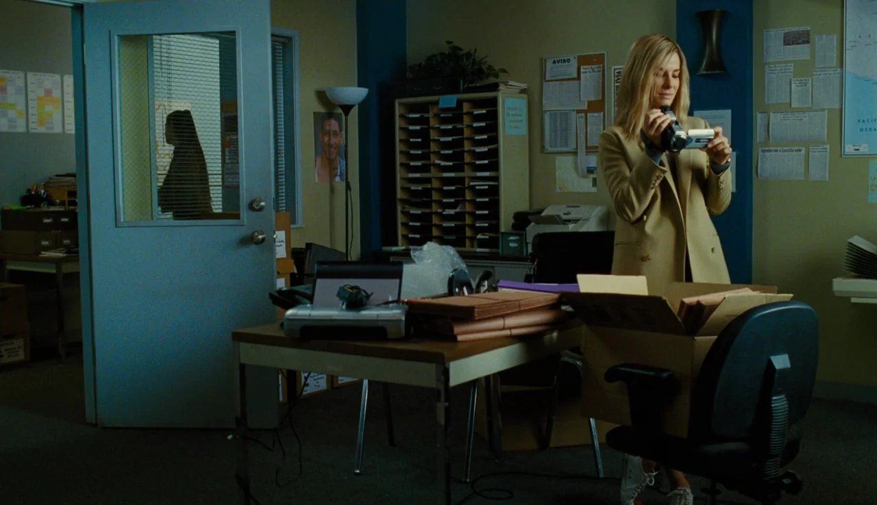 Our Brand is Crisis (2015) movie still: medium — A cluttered office features a desk with papers and folders near a blue door. A blonde woman stands…