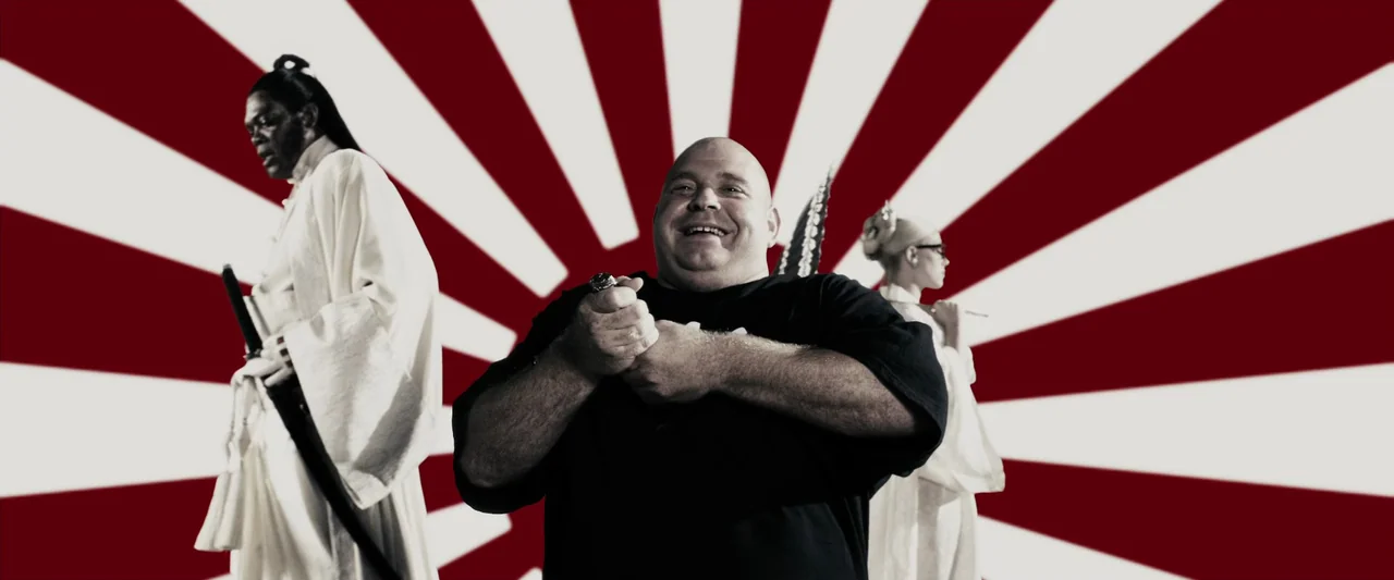 The Spirit (2008) movie still: medium — A studio environment with a prominent red and white Japanese sunburst graphic backdrop. Three people pose in…