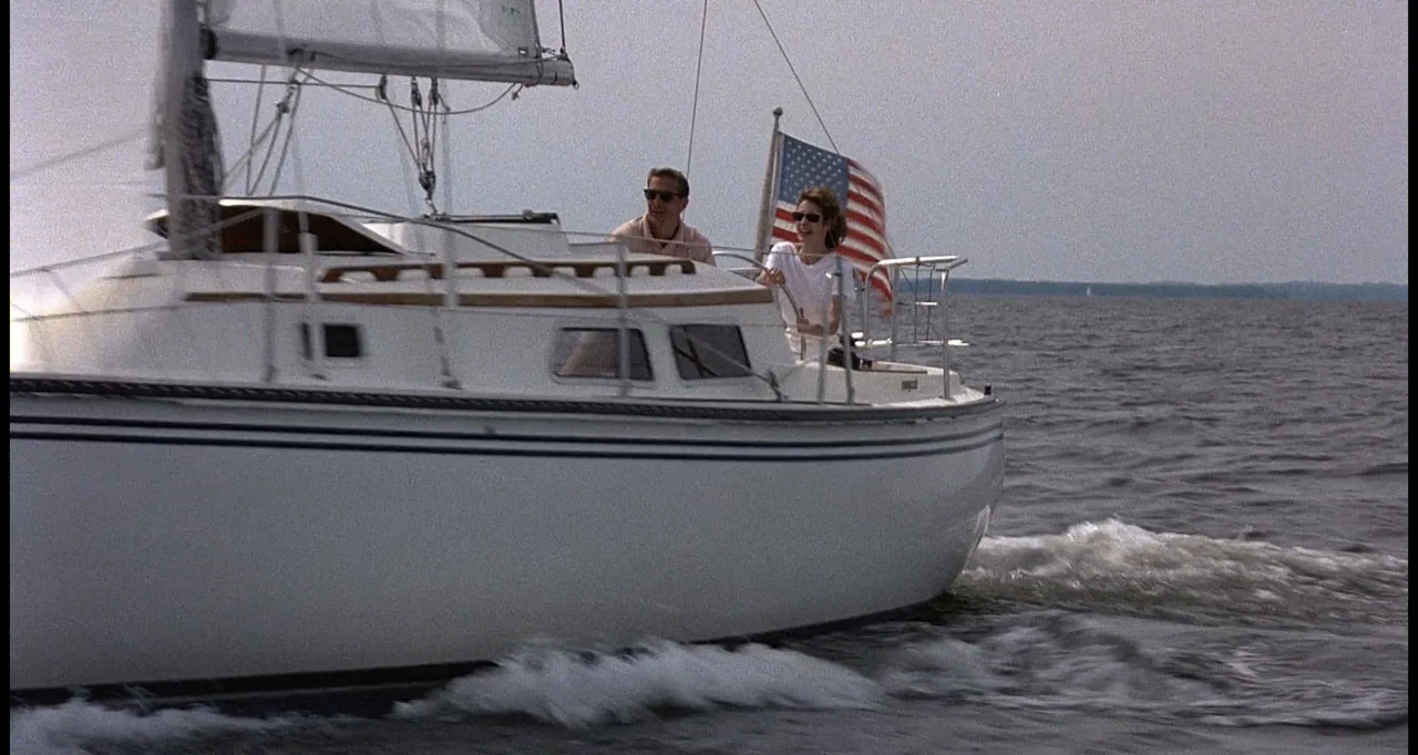 No Way Out (1987) movie still: wide — A white sailboat moves across a calm body of water under a bright sky. A man and a woman sit in the cockpit of…