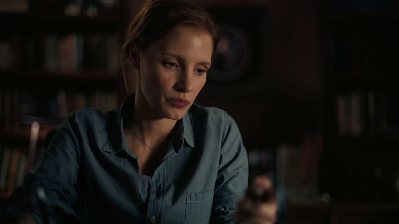 Interstellar (2014) movie still: medium — A woman sits inside a dimly lit room with rows of shelves blurred in background. She holds a small,…
