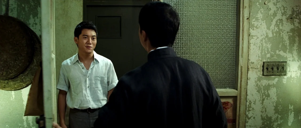 Ip Man 2 (2010) movie still: medium — A narrow apartment entryway features peeling green paint and a textured glass door panel. One man faces the…