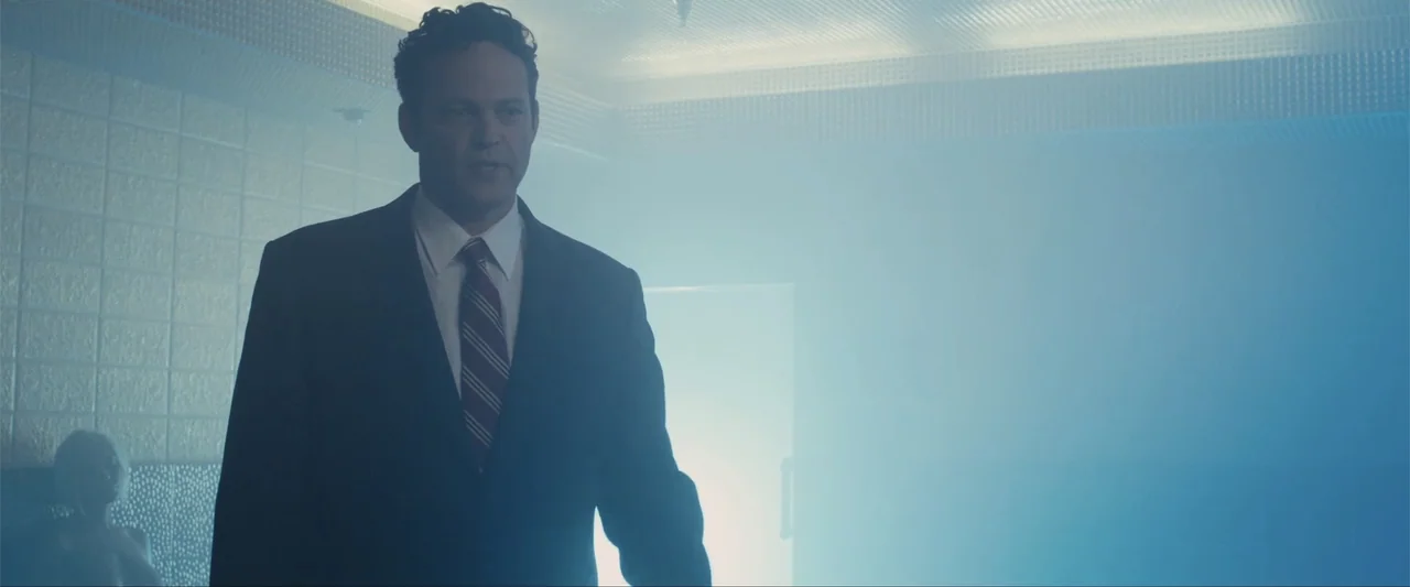 Unfinished Business (2015) movie still: medium — A tiled room is filled with dense white steam and cool blue light. A man wearing a business suit…