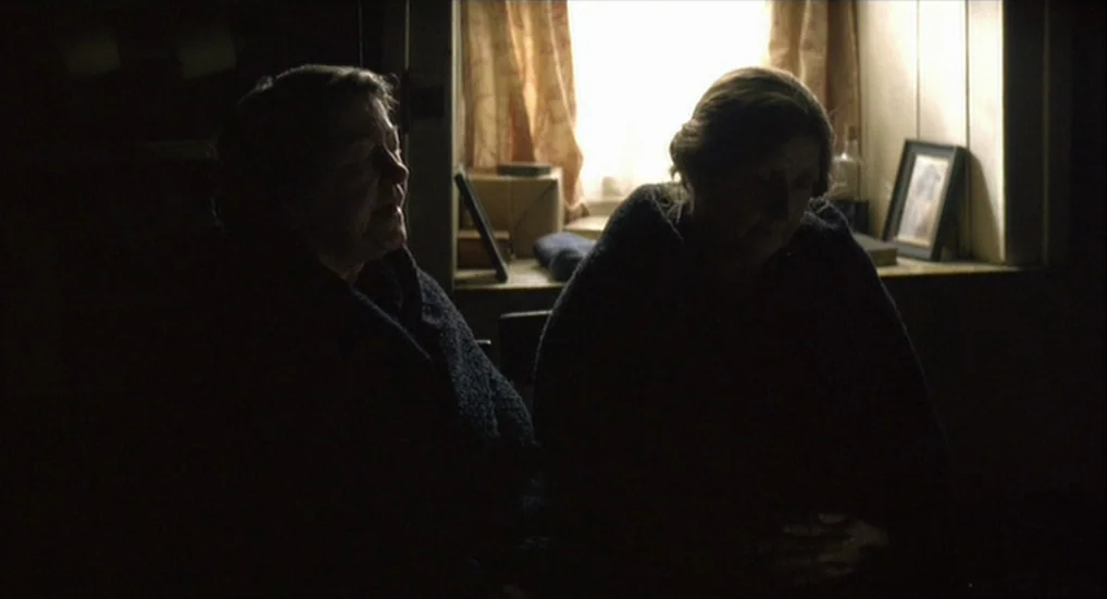 The Wind That Shakes the Barley (2006) movie still: medium — A dimly lit room features two women sitting in front of a window. They are wrapped in…