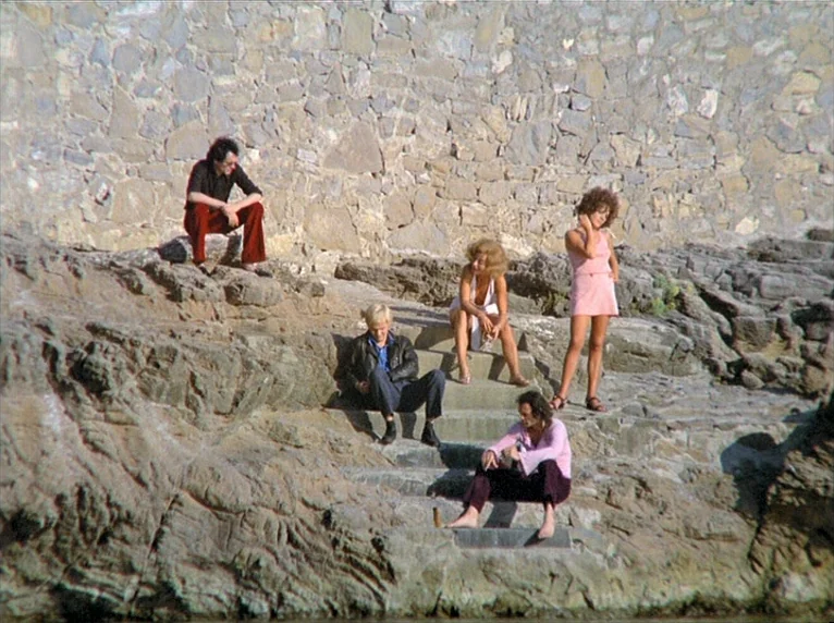 Beware Of A Holy Whore (1971) movie still: wide — A rugged cliffside features stone steps built into the face of a wall. Five people sit and stand…