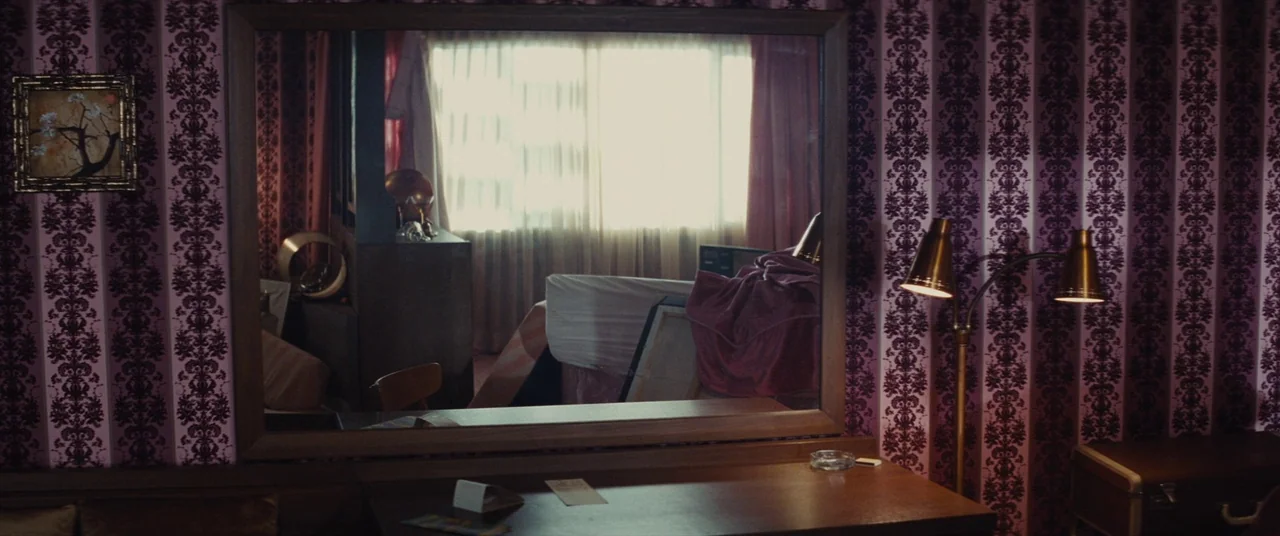 Bad Times at the El Royale (2018) movie still: medium — A 1970s motel room features heavy purple floral wallpaper and a wooden vanity mirror. The…