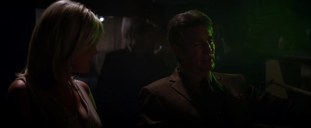 The Dark Knight (2008) movie still: medium — A dark room with minimal light and obscured background figures in shadows. A man and a woman sit in a…