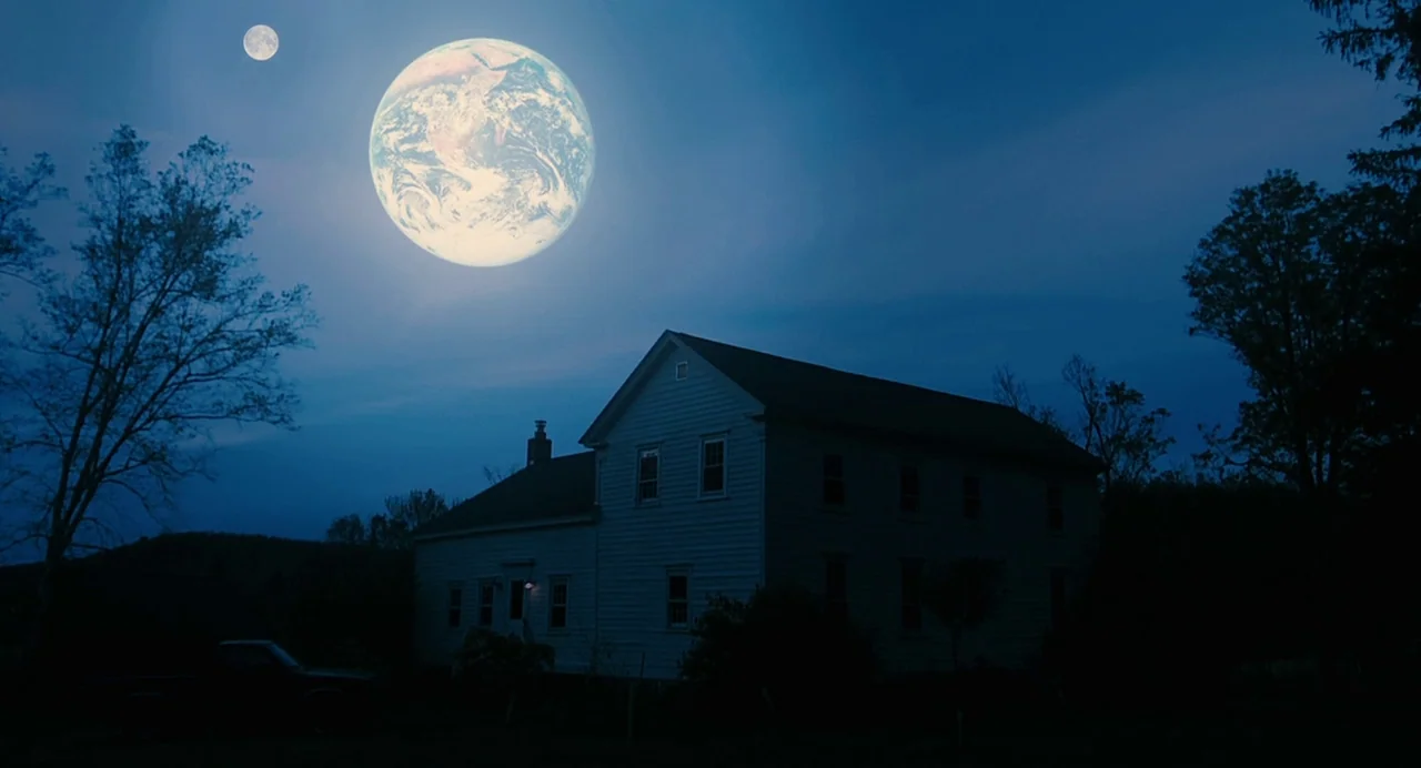 Another Earth (2011) movie still: wide — A two-story residential house sits in darkness beneath a vast night sky. A large luminous planet and a…
