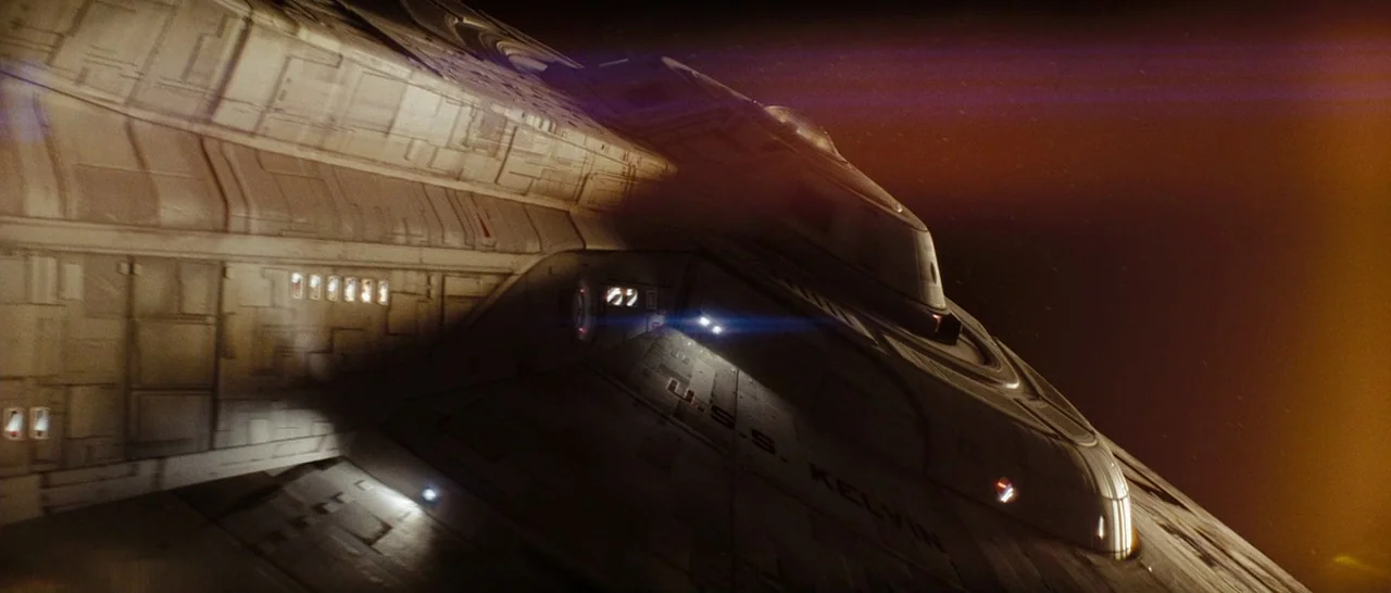 Star Trek (2009) movie still: wide — The saucer section of a large starship floats through the darkness of deep space. Text on the hull reads U.S.S.…