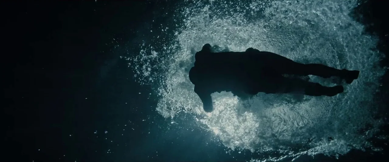 Death Note (2017) movie still: fullbody — A person swims horizontally through dark, deep water at night. White bubbles and wake surround the…