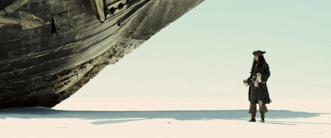 Pirates of the Caribbean: At World’s End movie still: wide — An immense wooden ship hull rests on a vast, flat, blindingly white salt plain. A…
