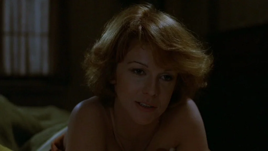 Magic (1978) movie still: closeup — A dimly lit room with bedding visible in the foreground. A woman lies in bed, her upper torso facing the camera.