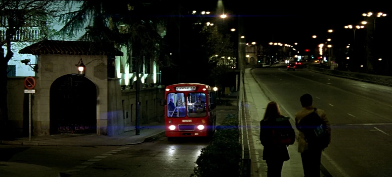 Live Flesh (1997) movie still: wide — A night city street features a red bus at a curb and a sidewalk. A young couple walks away from the camera…