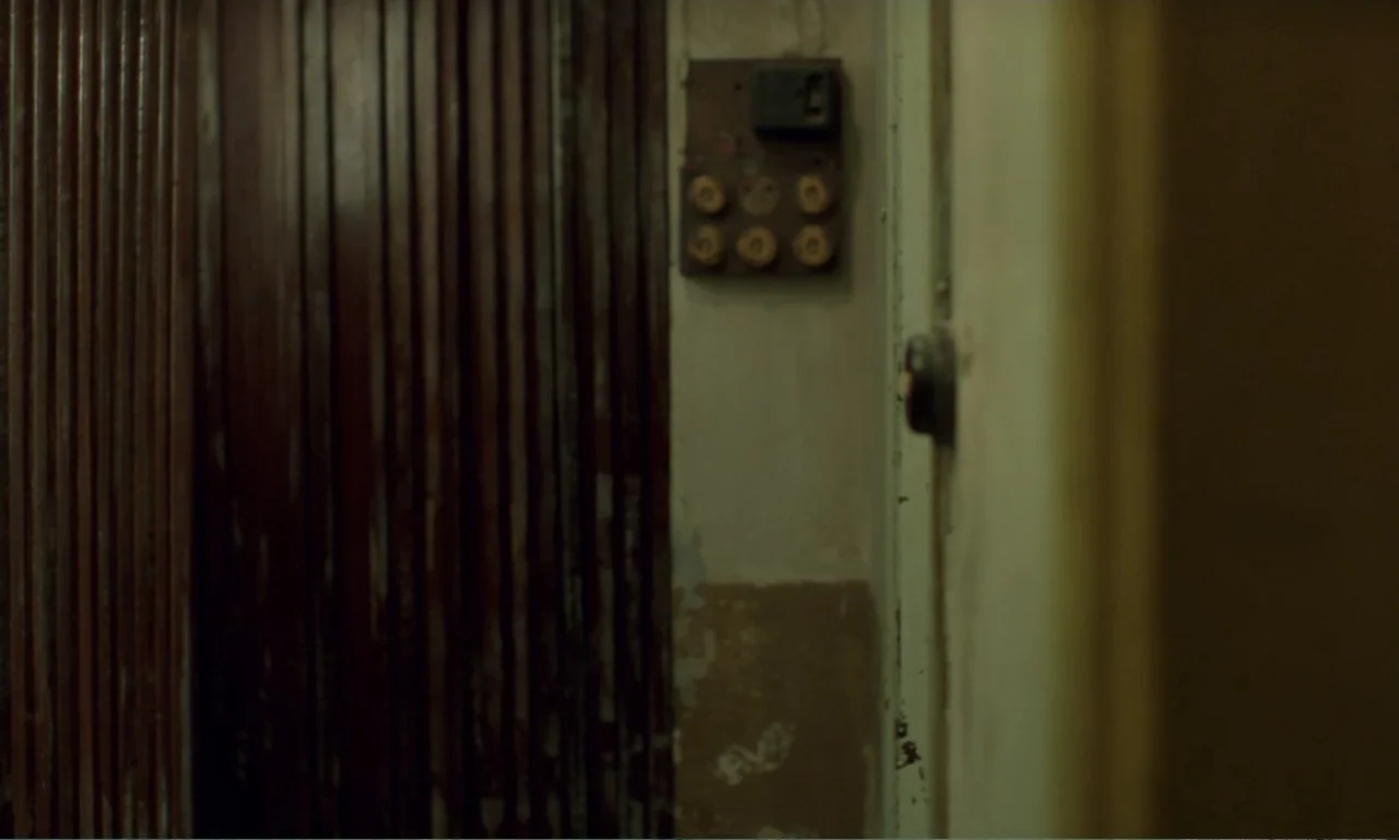 In the Mood for Love (2000) movie still: establishing — An aging interior wall features vertical dark wood slats beside a textured plaster surface.…