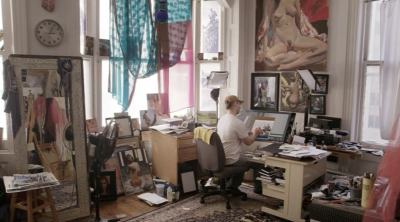 The Divided Soul of America (2019) movie still: medium — A cluttered artist studio contains multiple paintings, a drafting table, and various…
