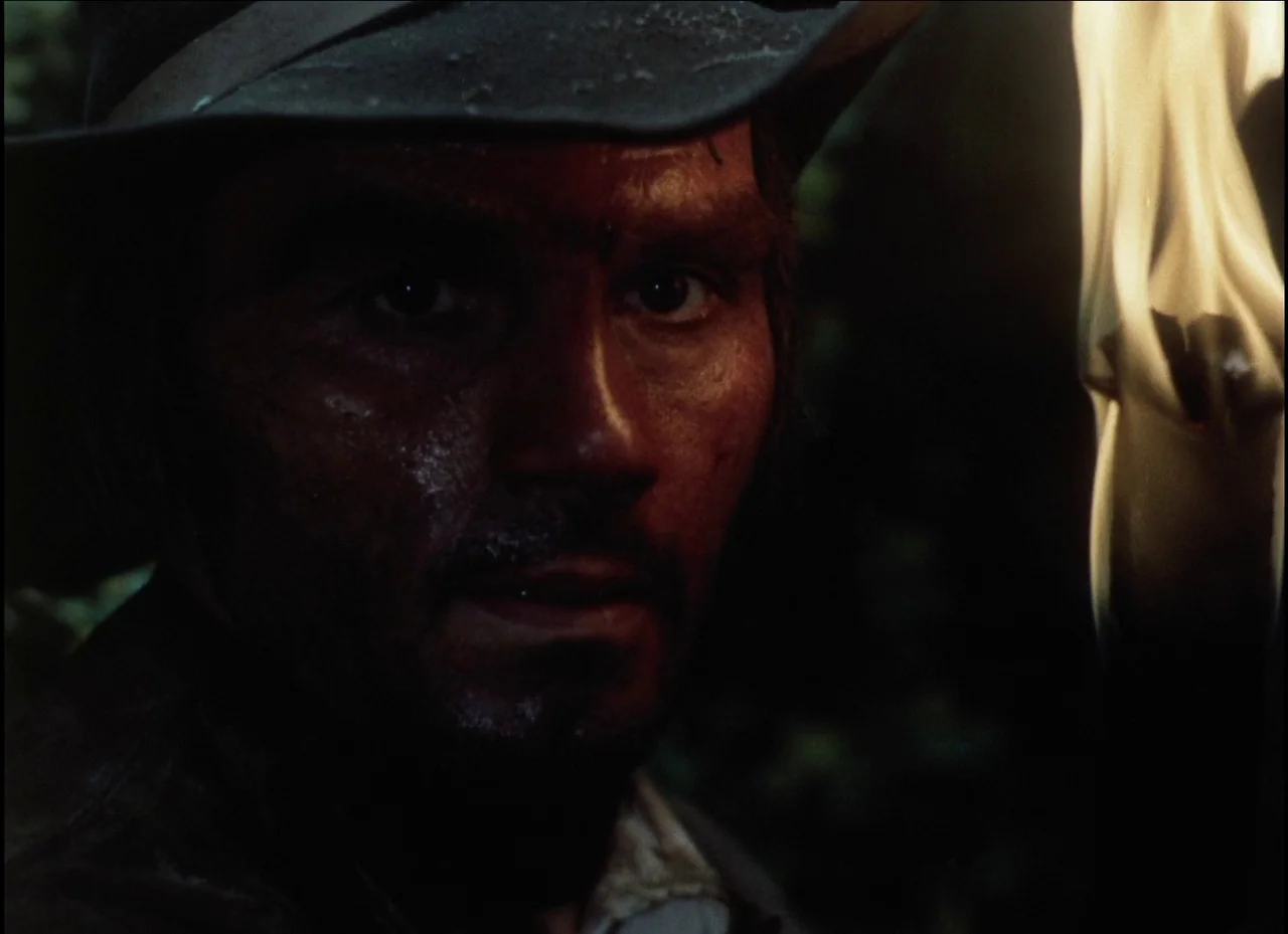 Beauty and the Beast (1979) movie still: closeup — A dark outdoor setting surrounded by dense foliage at night. A man with a dirty face holds a…