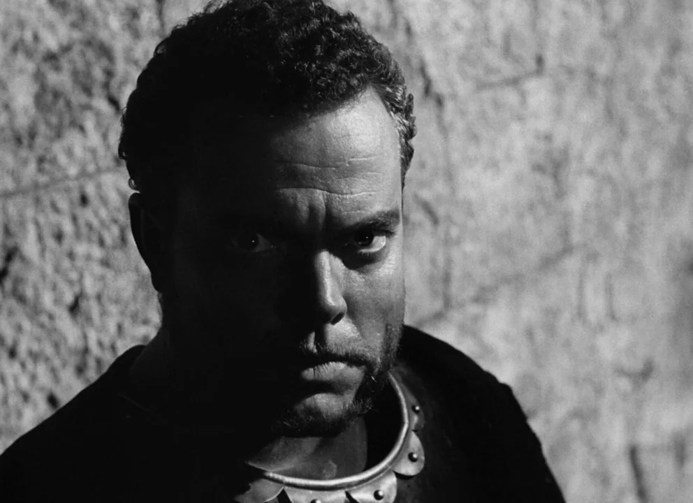 Othello (1952) movie still: closeup — A man stands close to a rough, weathered stone wall in medieval attire. The subject stares directly at the…