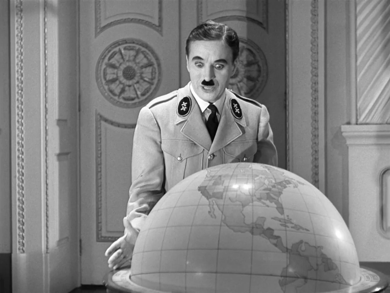 The Great Dictator (1940) movie still: medium — A man stands before a large, prominent globe in a formal indoor setting. He leans forward with wide…