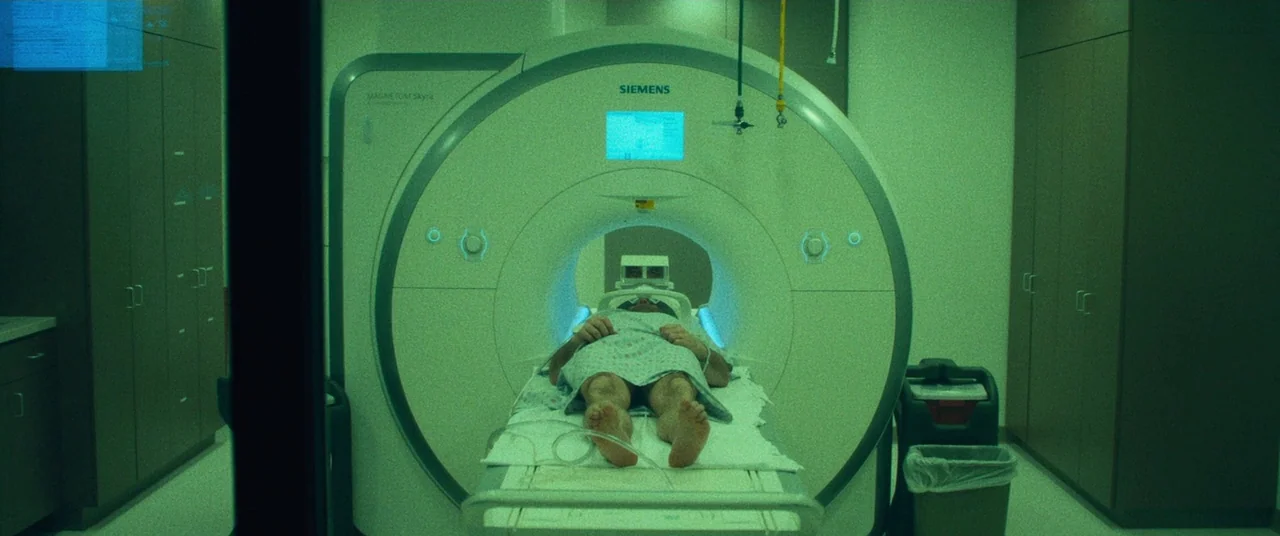 Dark Waters (2019) movie still: wide — A clinical room features a large, central white Siemens MRI machine with integrated screens. A person wearing…