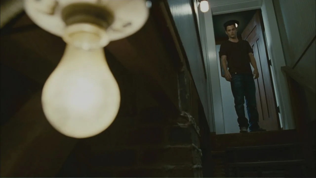 The Stepfather (2009) movie still: medium — A dark wooden staircase interior features a prominent out-of-focus light bulb hanging in the foreground.…