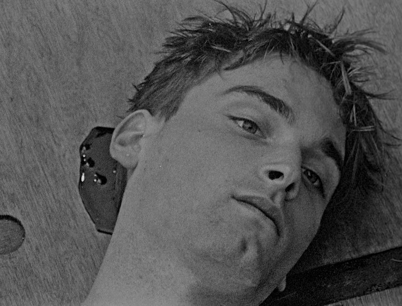 Bait (2019) movie still: closeup — A wooden pillory with a circular opening holds a man's head in place. The man looks forward toward the camera…
