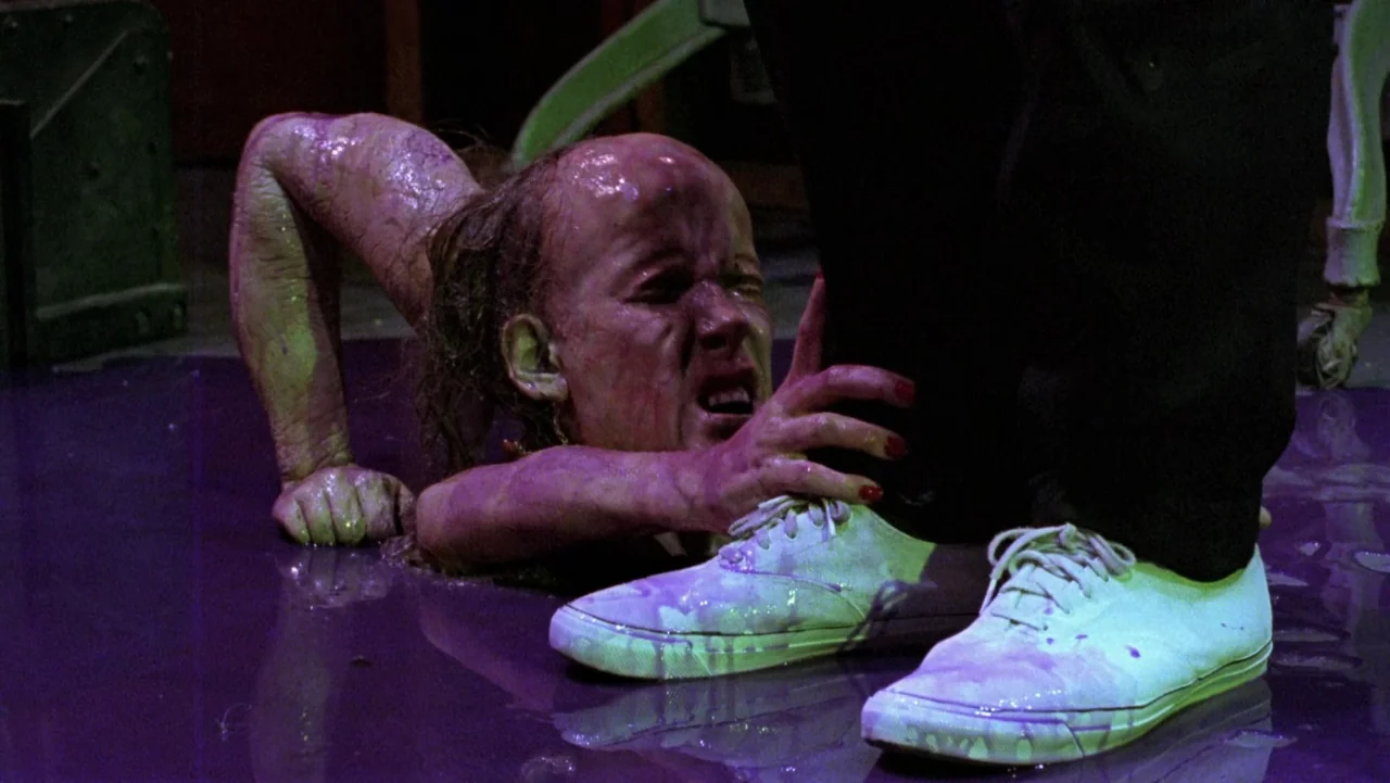 Frankenhooker (1990) movie still: medium — A dark indoor space is covered in a pool of viscous, dark purple liquid. A slime-covered mutant crawls…