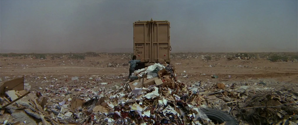 The Getaway (1972) movie still: wide — A vast, dusty landfill stretches under a hazy sky with scattered debris everywhere. A person stands on a…