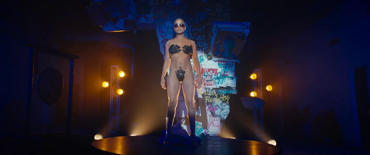 Sorry to Bother You (2018) movie still: fullbody — A dark, graffiti-covered pillar stands behind a circular platform in a dimly lit studio. A woman…