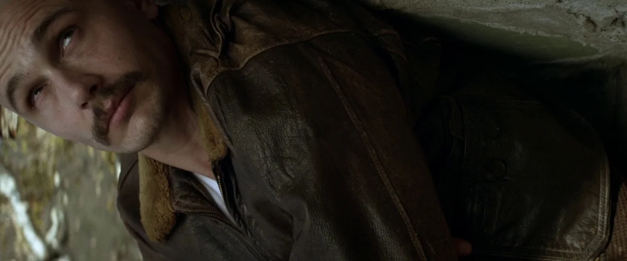 Zeroville (2019) movie still: closeup — A close-up captures a man lying against a textured, gray concrete surface. The subject wears a vintage…