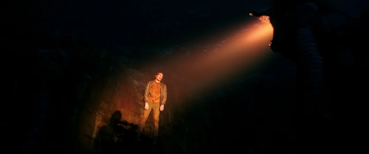 It Chapter Two (2019) movie still: wide — A man stands inside a dark, rocky enclosure during the night. A sharp, bright orange light hits him from…