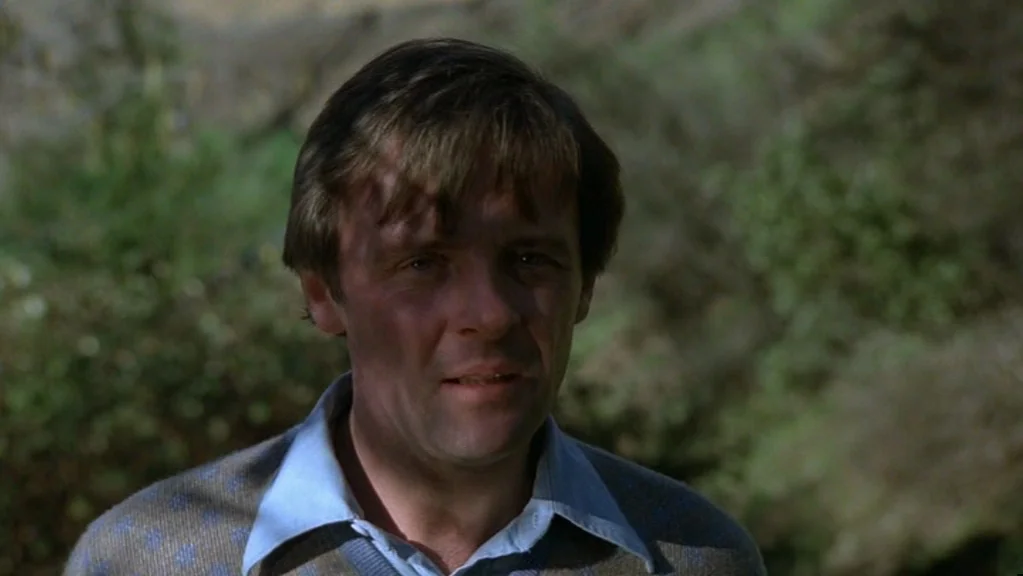 Magic (1978) movie still: closeup — A man stands outdoors with a blurred hillside of grass and foliage behind him. The person looks toward the…