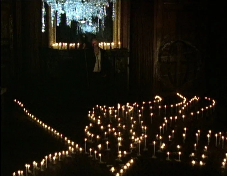 The Tempest (1979) movie still: wide — A dark, wood-paneled room features a massive chandelier reflected in a large mirror. Hundreds of small white…