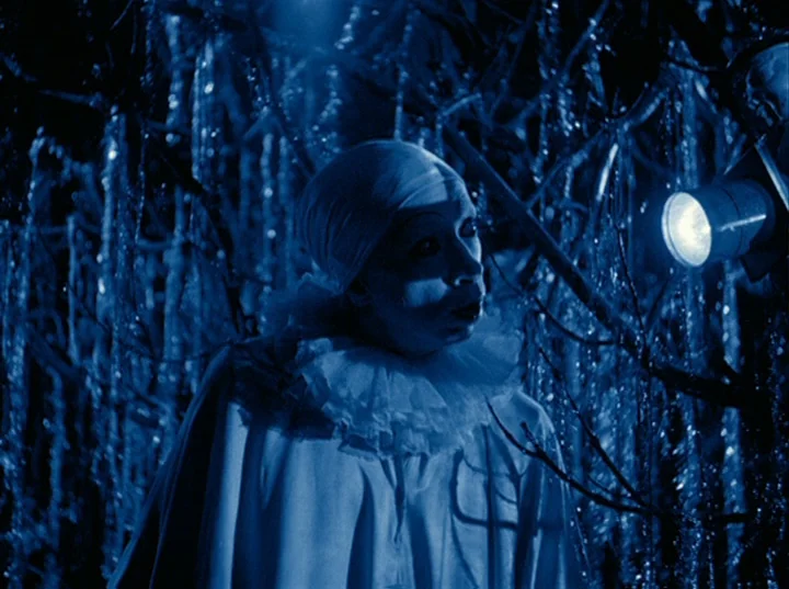 Rabbit’s Moon (1950) movie still: medium — A figure dressed as a clown stands amidst dark, intertwined branches in the night. The clown gazes at a…