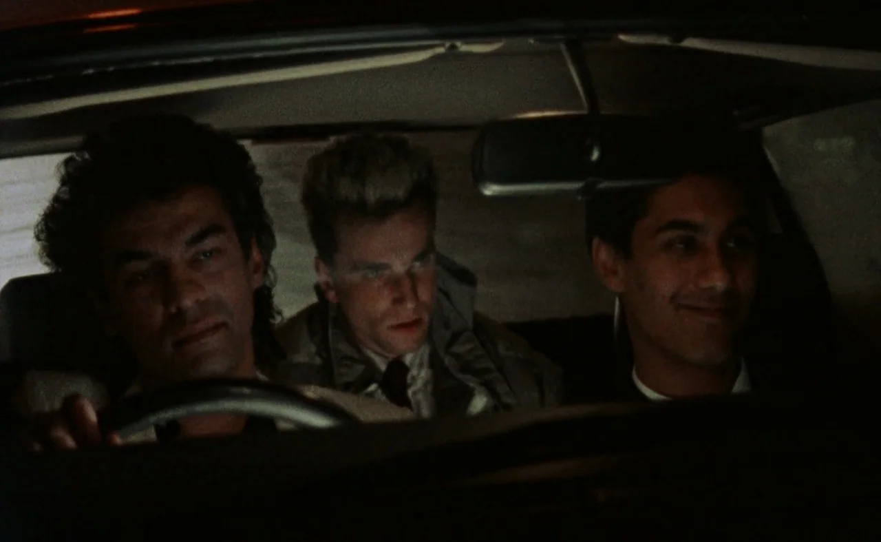 My Beautiful Laundrette (1985) movie still: medium — Three men are crowded into the front seat of a car at night. The man on the left drives while…