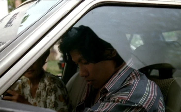 Blissfully Yours (2002) movie still: medium — Two people sit in the front seats of a vehicle viewed through the window. The man in the foreground…