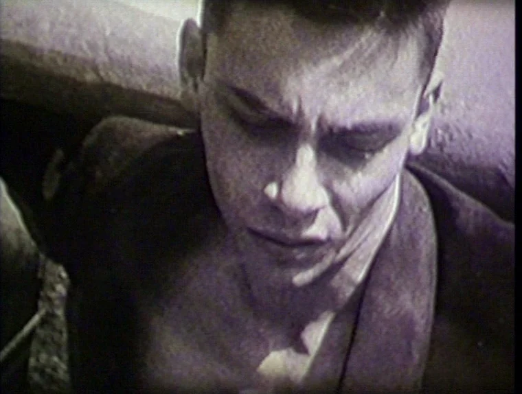 The Angelic Conversation (1985) movie still: closeup — A close-up view shows a man inside a dimly lit confined space. The man tilts his head…