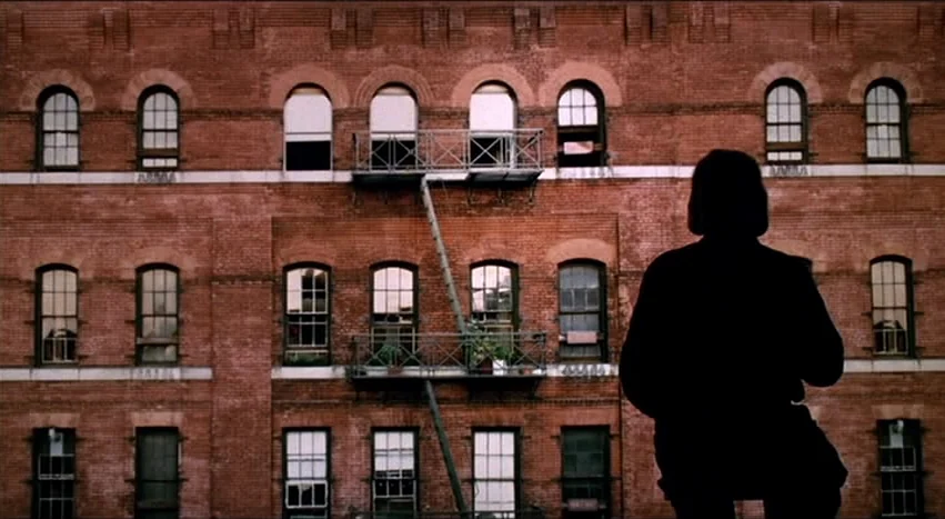 Gray’s Anatomy (1996) movie still: medium — A brick tenement building facade features a centered steel fire escape with small potted plants. A…