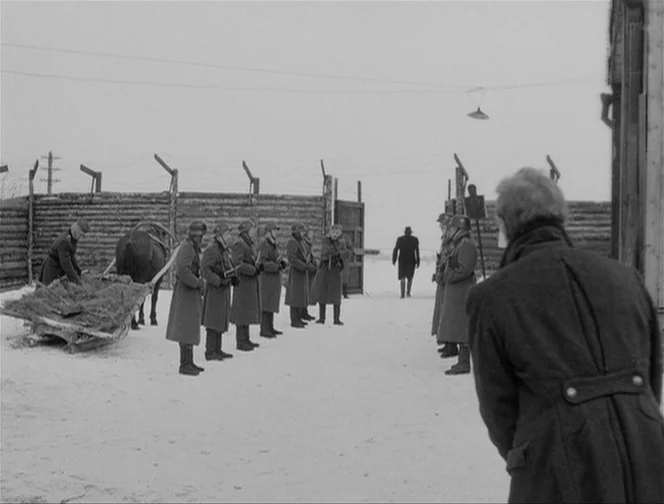 The Ascent (1977) movie still: wide — A snow-covered military compound features a perimeter fence made of thick logs and wire. A row of soldiers in…