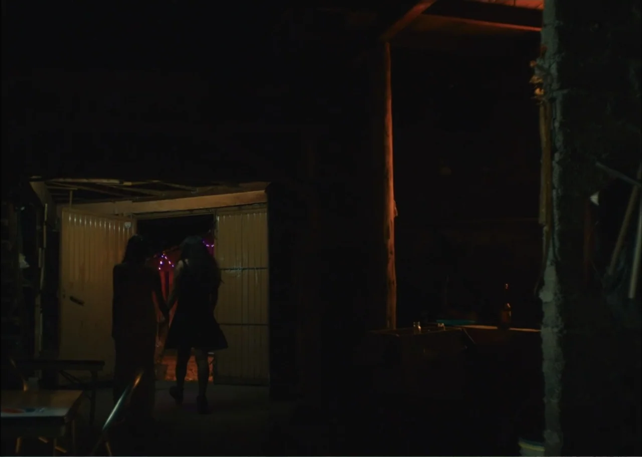 A Fisherman's Tale (1976) movie still: fullbody — A dark interior with concrete pillars and a partially opened metal garage door. Two women walk…