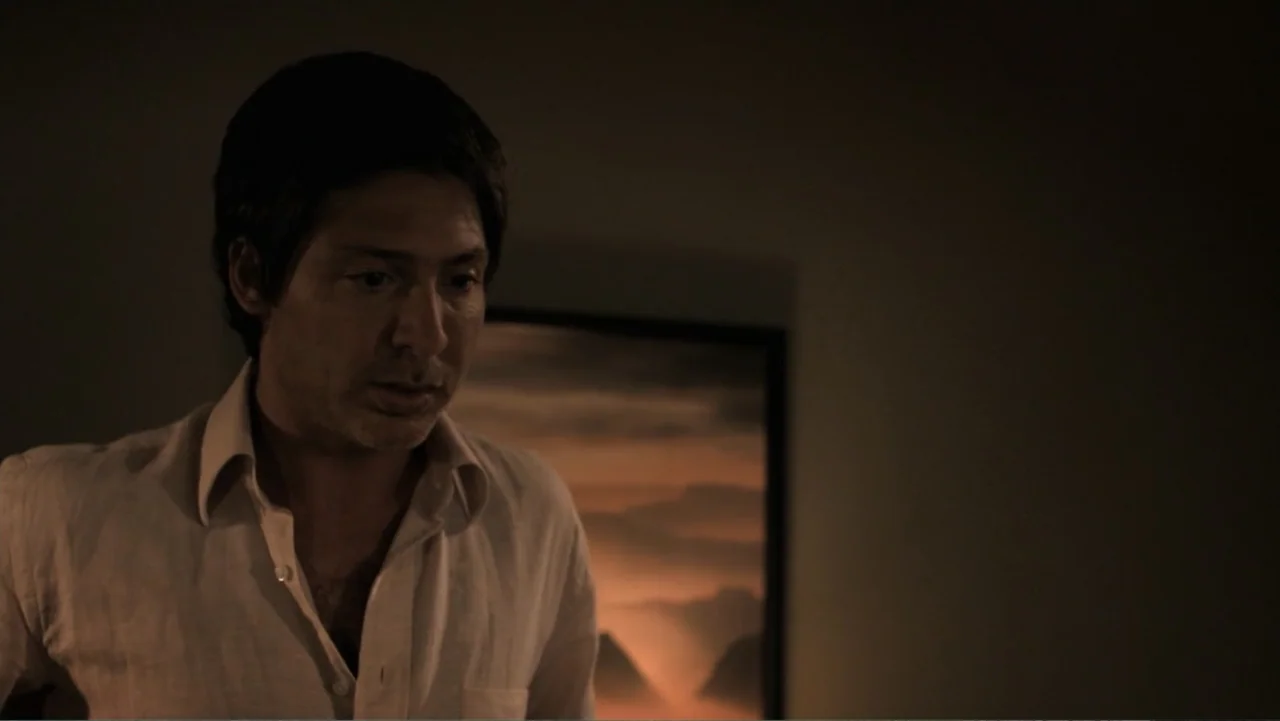 A Boyfriend for My Wife (2008) movie still: medium — A dimly lit interior space features a framed landscape painting on a dark wall. A man in an…