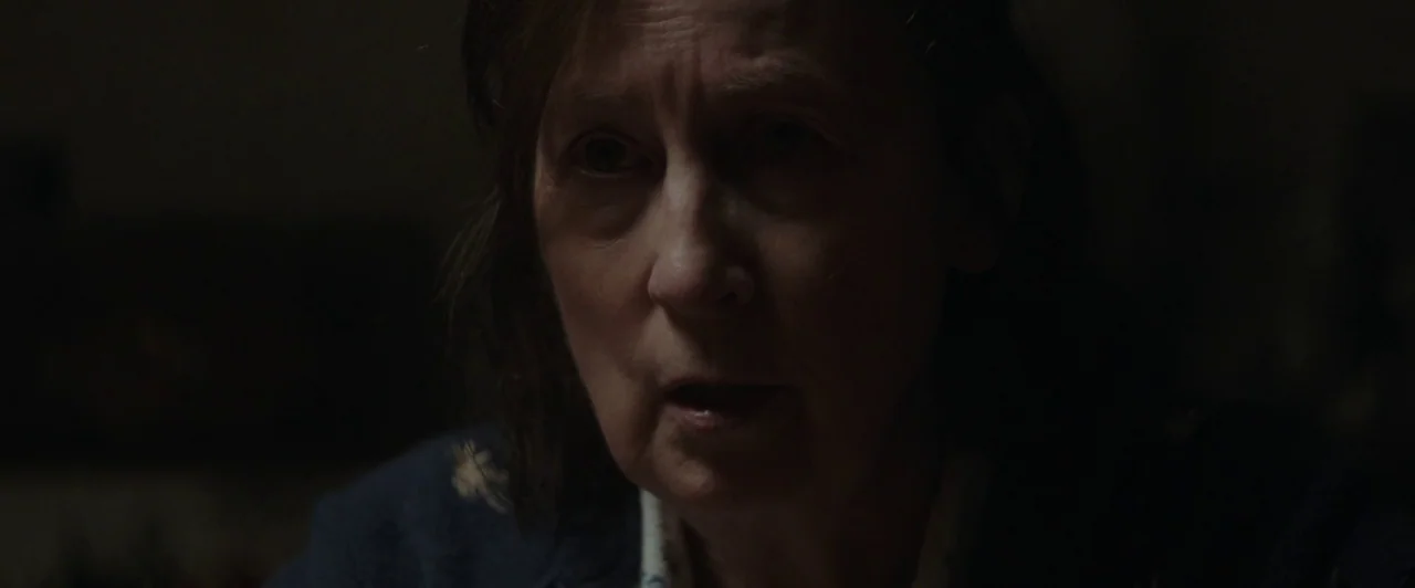 You Are Not My Mother (2021) movie still: closeup — A dimly lit indoor space with low light levels and deep shadows. An elderly woman with brown…