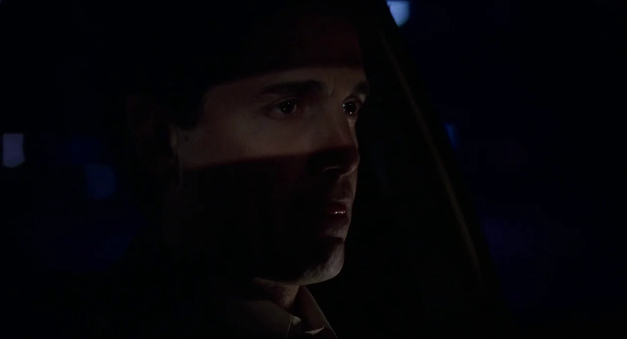 Child’s Play (1988) movie still: closeup — The interior of a moving vehicle at night with darkness encompassing the surroundings. A man sits in the…