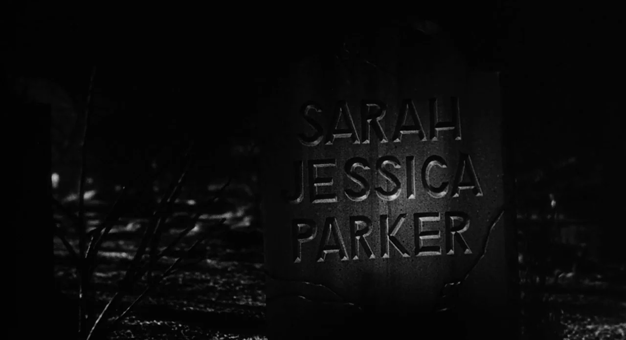 Ed Wood (1994) movie still: closeup — A dark, textured stone headstone stands in a cemetery at night. The name Sarah Jessica Parker is carved in…