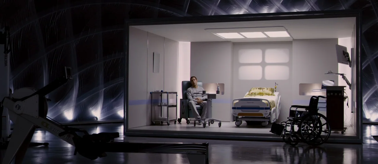 Self/less (2015) movie still: wide — A sterile, white-walled medical cubicle sits isolated within a vast, dark, cavernous industrial space. A lone…