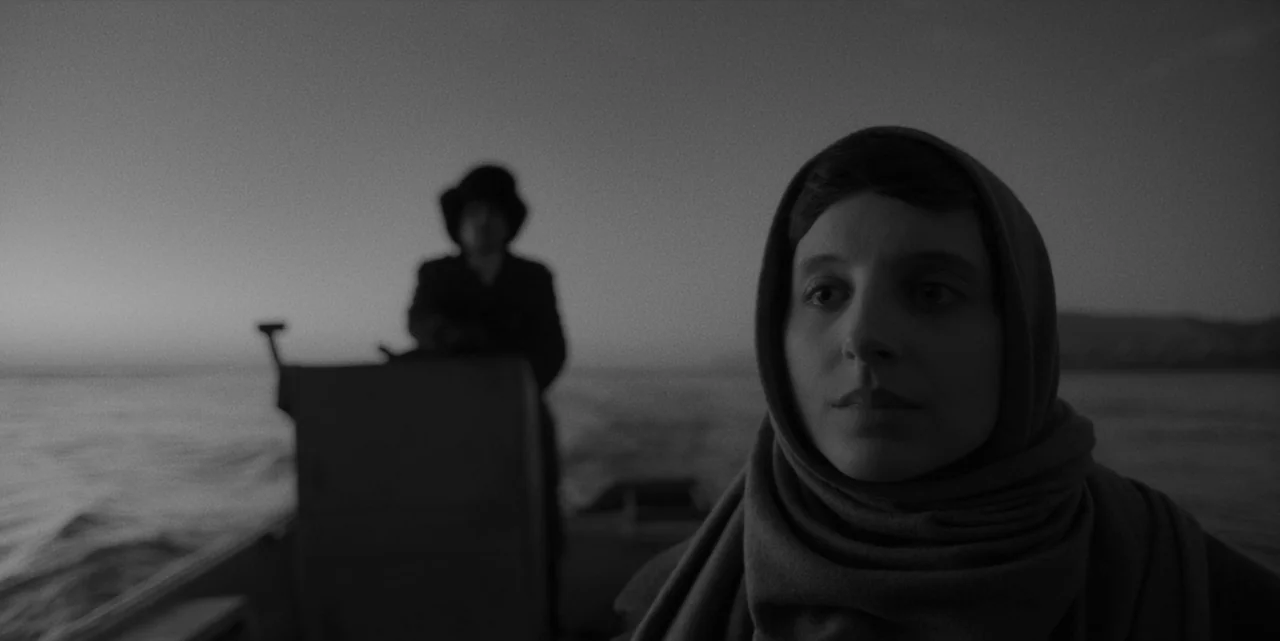 El Conde (2023) movie still: medium — A boat travels across a dark body of water under a dim twilight sky. A woman in a headscarf sits in the…