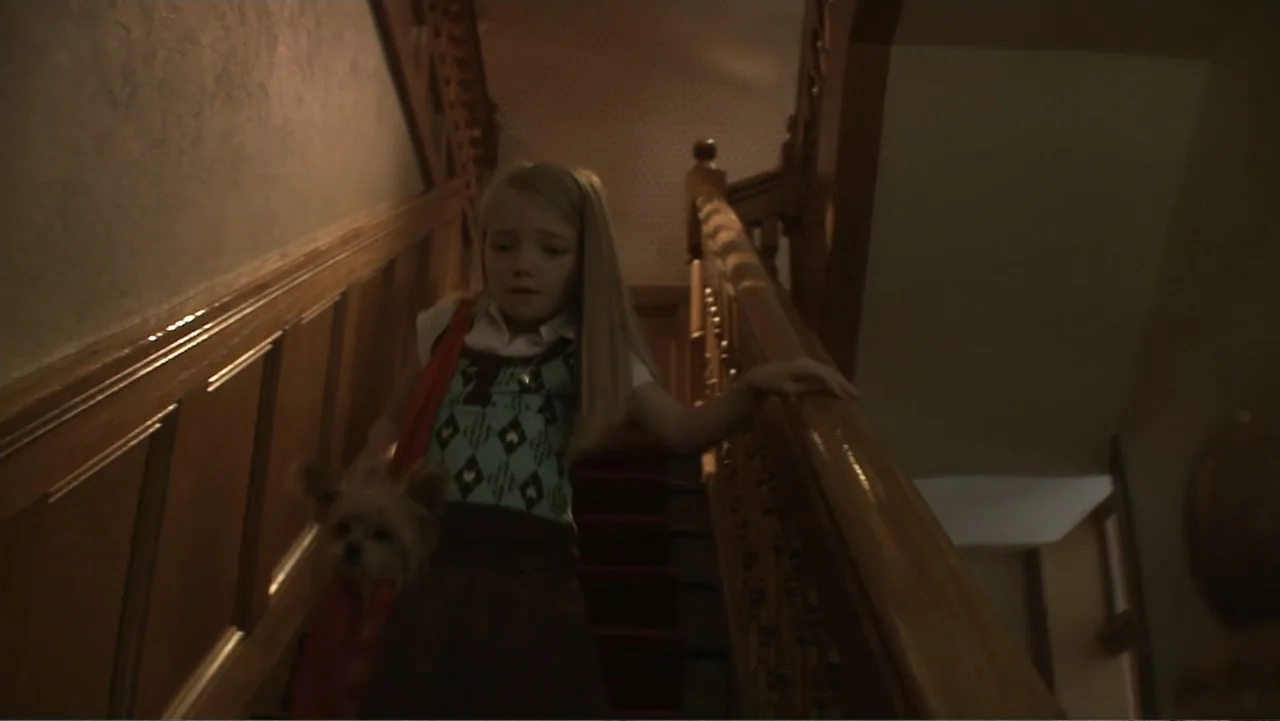 Boathouse Detectives (2010) movie still: medium — A dark wooden staircase features a red runner and heavy carved banisters. A young girl with long…