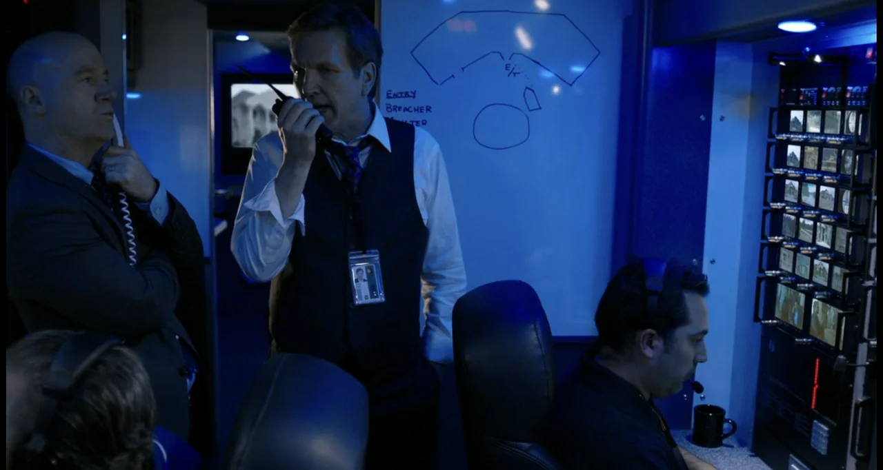 Sabotage (2014) movie still: medium — A cramped surveillance vehicle filled with multiple glowing monitors and white strategy boards. Three men in…