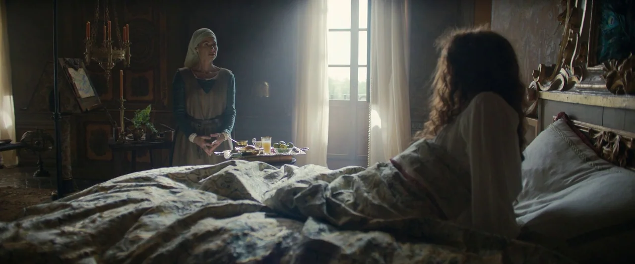 Rosaline (2022) movie still: medium — A dimly lit period bedroom features wood-paneled walls and a window with white curtains. A woman in an apron…