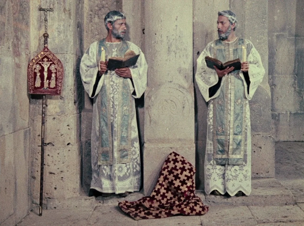 The Colour of Pomegranates (1969) movie still: fullbody — An interior stone cathedral wall features carved pillars and a central patterned textile.…